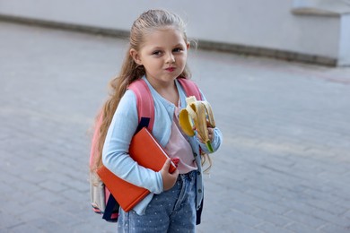 Photo of Cute little girl eating banana outdoors. School lunch
