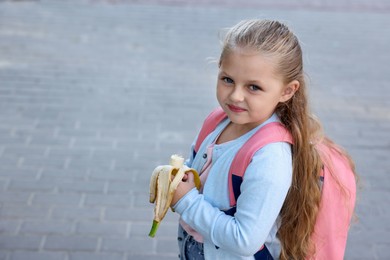 Photo of Cute little girl eating banana outdoors, space for text. School lunch