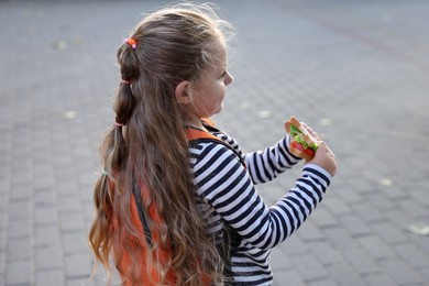 Photo of Cute little girl eating sandwich outdoors. School lunch