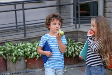 Photo of Cute little kids eating apples outdoors, space for text. School lunch