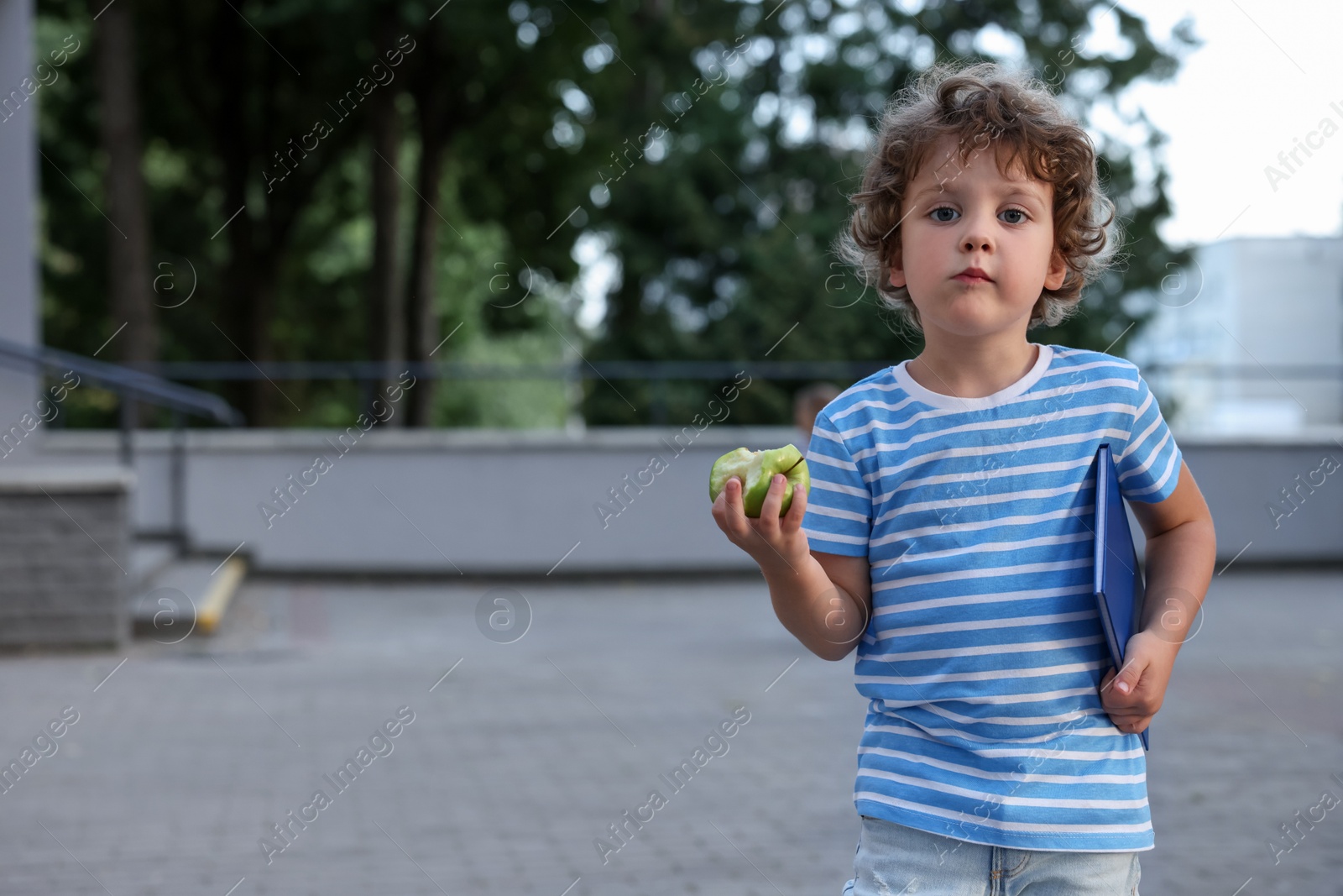 Cute little boy eating apple outdoors, space for text. School lunch Photo of Cute little boy eating apple outdoors, space for text. School lunch