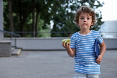 Photo of Cute little boy eating apple outdoors, space for text. School lunch