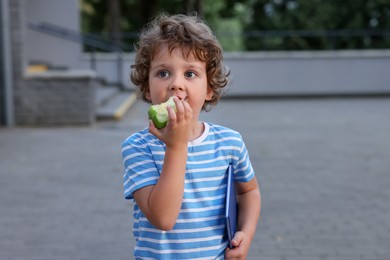 Photo of Cute little boy eating apple outdoors. School lunch