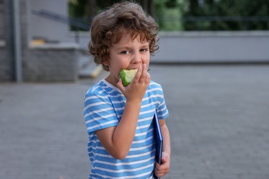 Photo of Cute little boy eating apple outdoors. School lunch