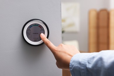 Photo of Woman adjusting hygrometer on white wall indoors, closeup. Smart home system