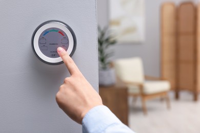 Photo of Woman adjusting hygrometer on white wall indoors, closeup and space for text. Smart home system