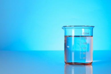 Photo of Glass beaker with dirty water on light blue background. Space for text