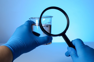 Photo of Scientist with magnifying glass and sample of water on light blue background, closeup