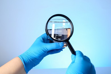 Photo of Scientist with magnifying glass and sample of water on light blue background, closeup