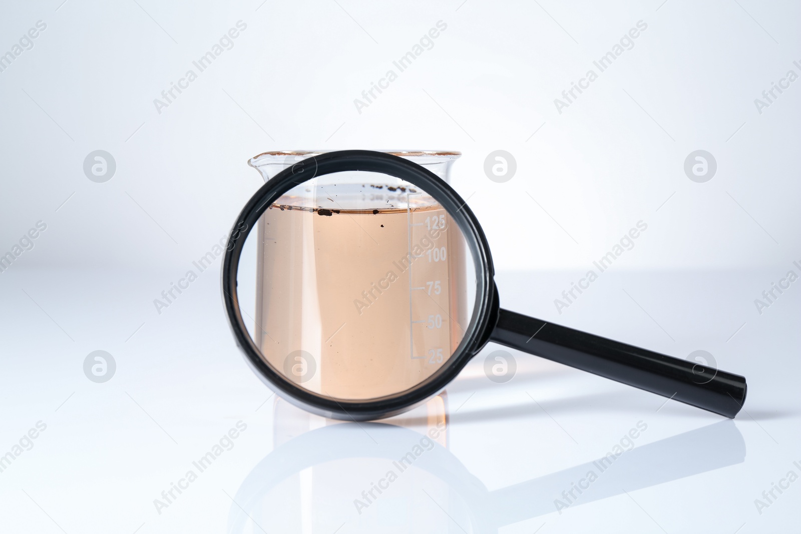 Photo of Beaker with dirty water and magnifying glass on white background