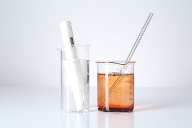 Photo of Clean and dirty water in beakers with quality meter on white background