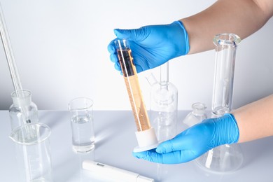 Photo of Scientist testing dirty water at white table, closeup
