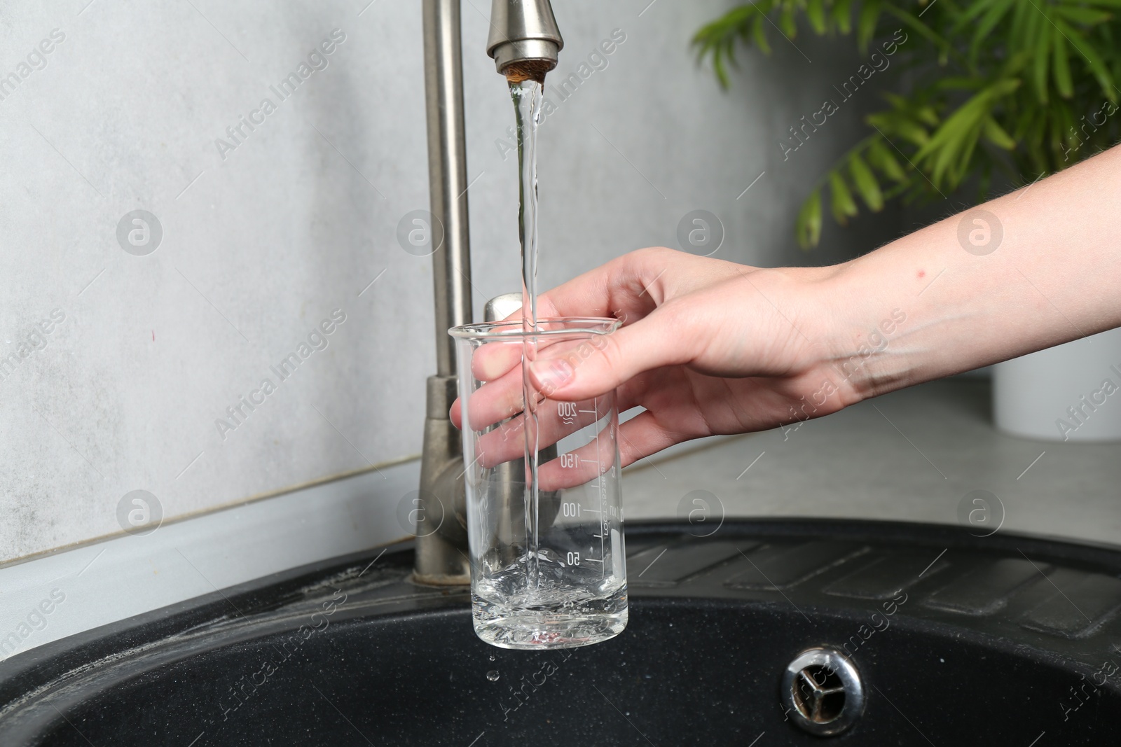 Woman taking sample of water from faucet indoors, closeup. Quality testing Photo of Woman taking sample of water from faucet indoors, closeup. Quality testing