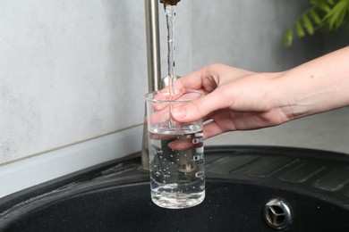 Photo of Woman taking sample of water from faucet indoors, closeup. Quality testing