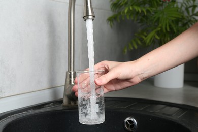 Photo of Woman taking sample of water from faucet indoors, closeup. Quality testing