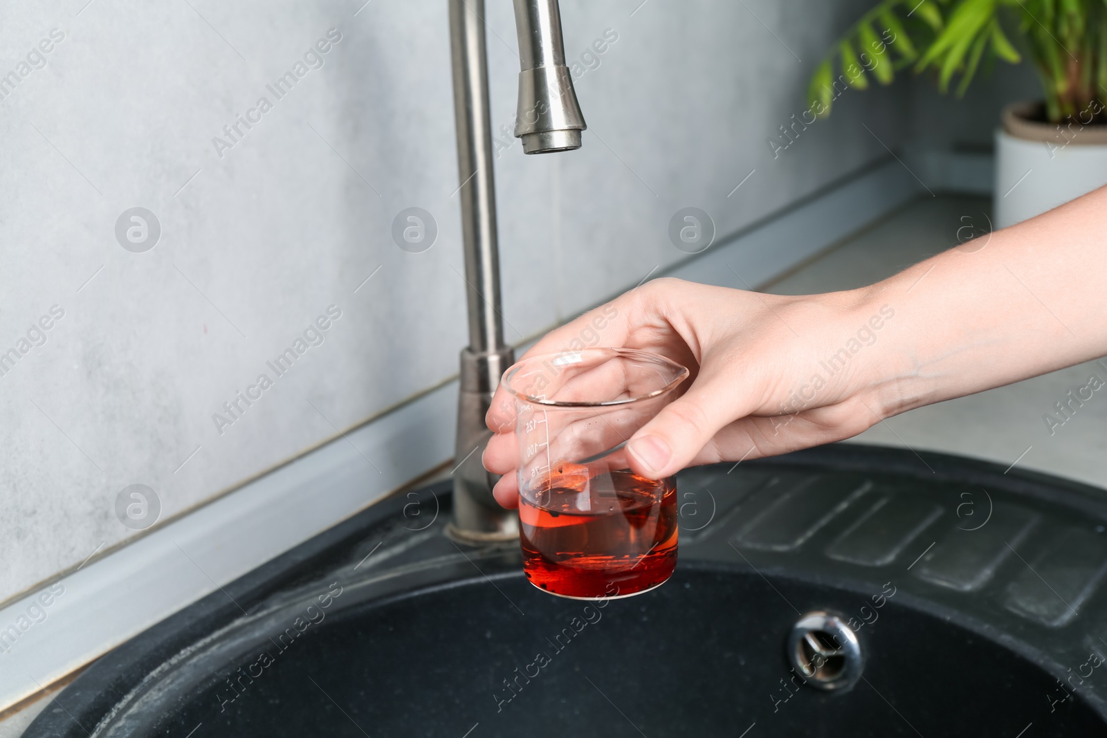 Photo of Woman taking sample of water from faucet indoors, closeup. Quality testing