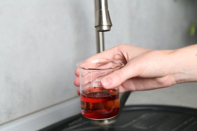 Photo of Woman taking sample of water from faucet indoors, closeup. Quality testing