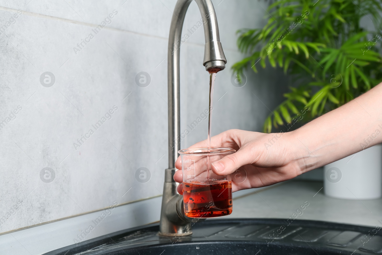 Photo of Woman taking sample of water from faucet indoors, closeup. Quality testing