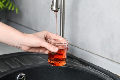 Photo of Woman taking sample of water from faucet indoors, closeup. Quality testing