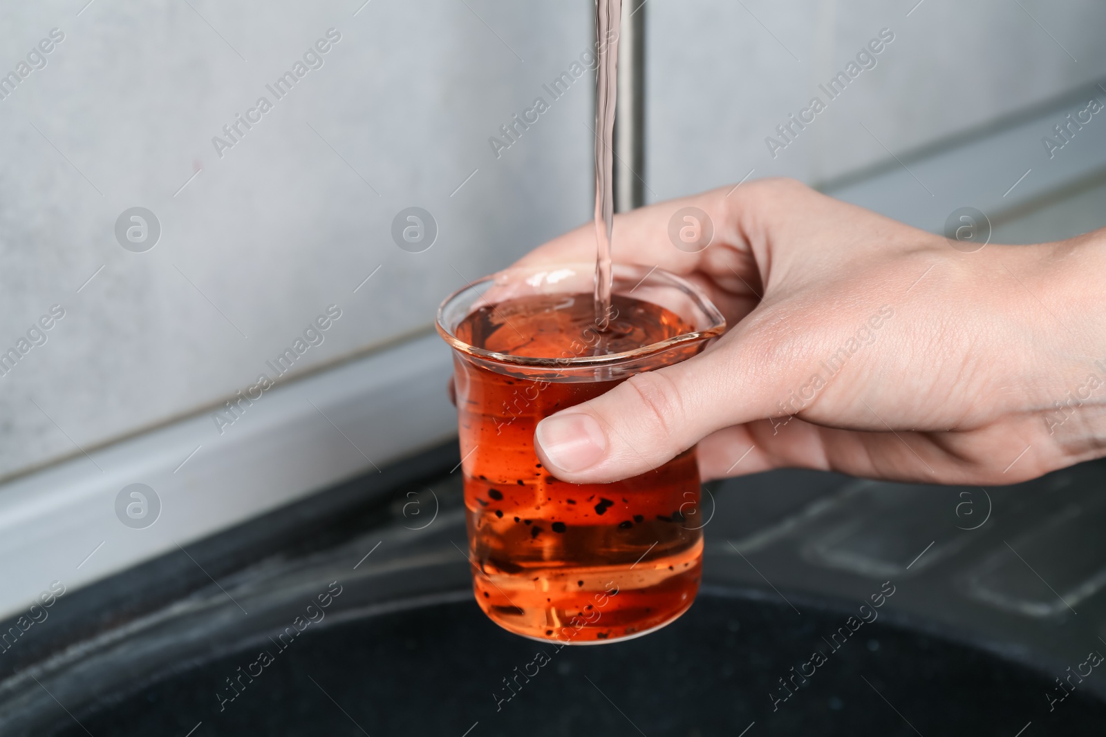 Photo of Woman taking sample of water from faucet indoors, closeup. Quality testing