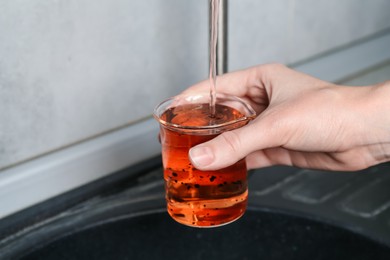 Photo of Woman taking sample of water from faucet indoors, closeup. Quality testing