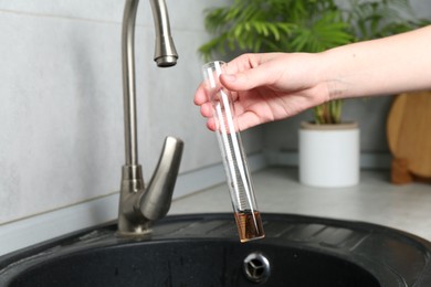 Photo of Woman taking sample of water from faucet indoors, closeup. Quality testing