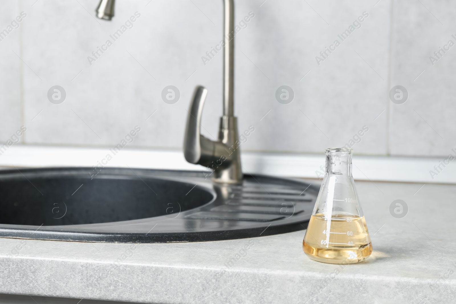 Photo of Sample of dirty water in flask near sink indoors