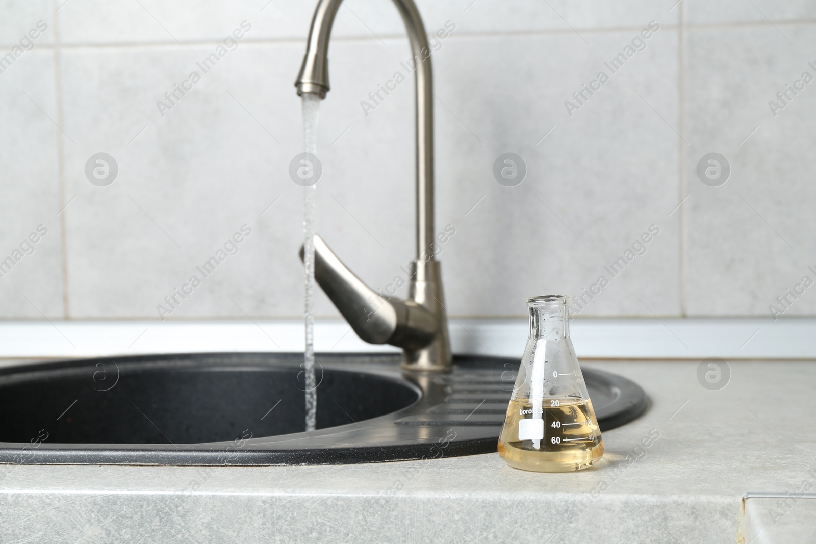 Sample of dirty water in flask near sink indoors Photo of Sample of dirty water in flask near sink indoors