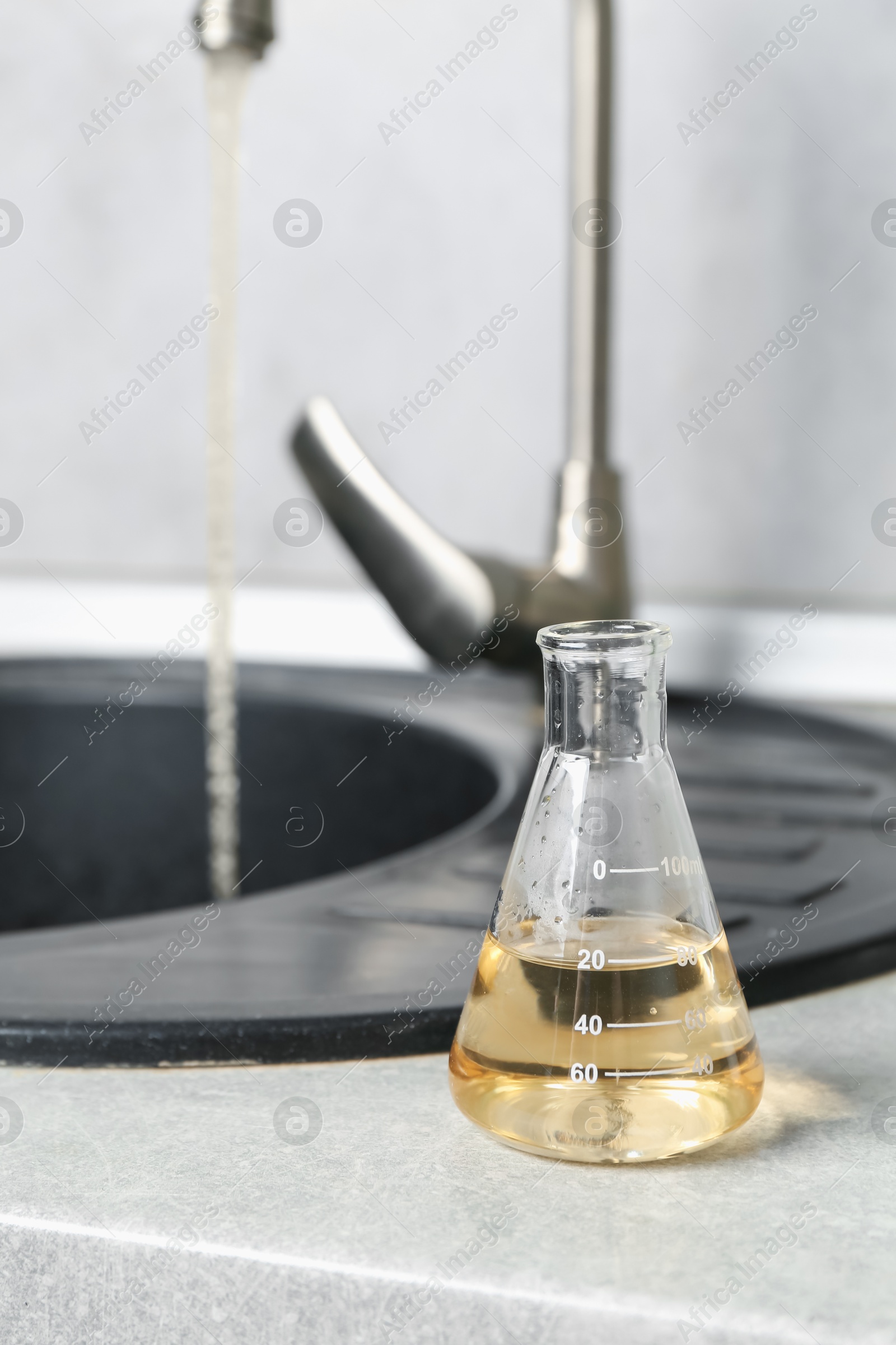 Sample of dirty water in flask near sink indoors Photo of Sample of dirty water in flask near sink indoors