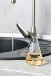 Photo of Sample of dirty water in flask near sink indoors