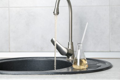Photo of Sample of dirty water in flask near sink indoors