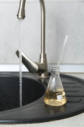 Photo of Sample of dirty water in flask near sink indoors