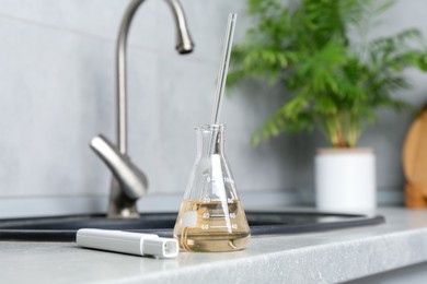 Photo of Sample of dirty water and quality meter near sink indoors