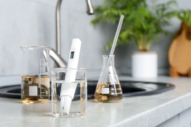 Photo of Samples of water and quality meter near sink indoors