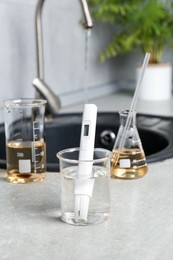 Photo of Samples of water and quality meter near sink indoors