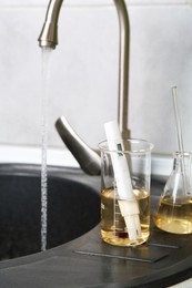 Photo of Samples of dirty water and quality meter near sink indoors