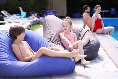 Photo of Cute kids resting in bean bag chairs near swimming pool outdoors, selective focus. Family vacation