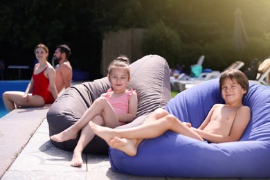 Photo of Cute kids resting in bean bag chairs near swimming pool outdoors, selective focus. Family vacation