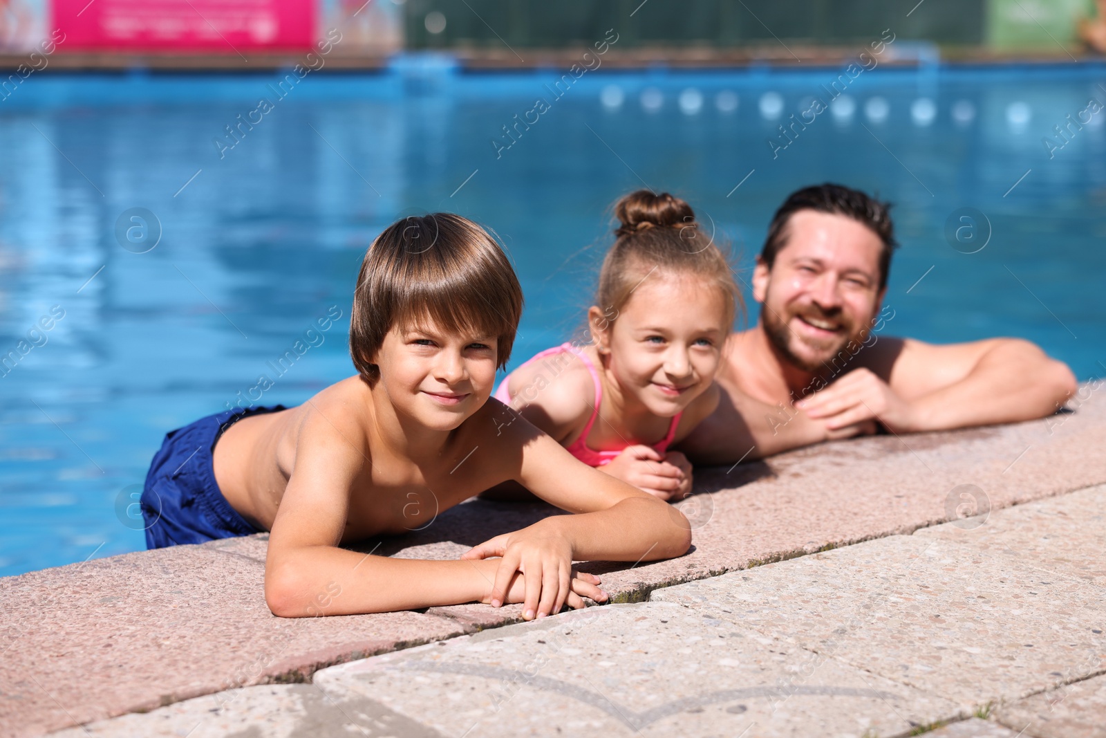 Photo of Happy father and his kids resting in swimming pool outdoors. Family vacation