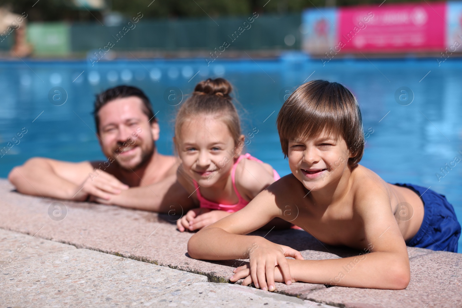 Photo of Happy father and his kids resting in swimming pool outdoors. Family vacation