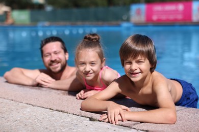 Photo of Happy father and his kids resting in swimming pool outdoors. Family vacation