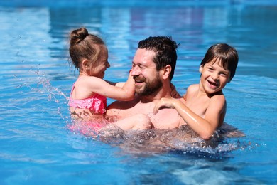 Photo of Happy father and his kids resting in swimming pool outdoors. Family vacation