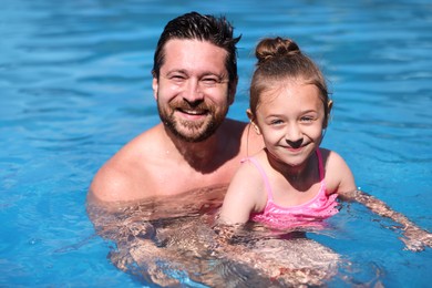 Photo of Happy father and his daughter resting in swimming pool outdoors. Family vacation