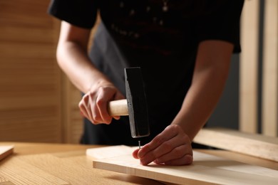 Photo of Man hammering nail into wooden plank indoors, closeup