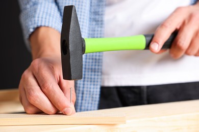 Photo of Man hammering nail into wooden plank indoors, closeup