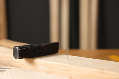 Photo of Metal nail in wooden plank and hammer on table, closeup