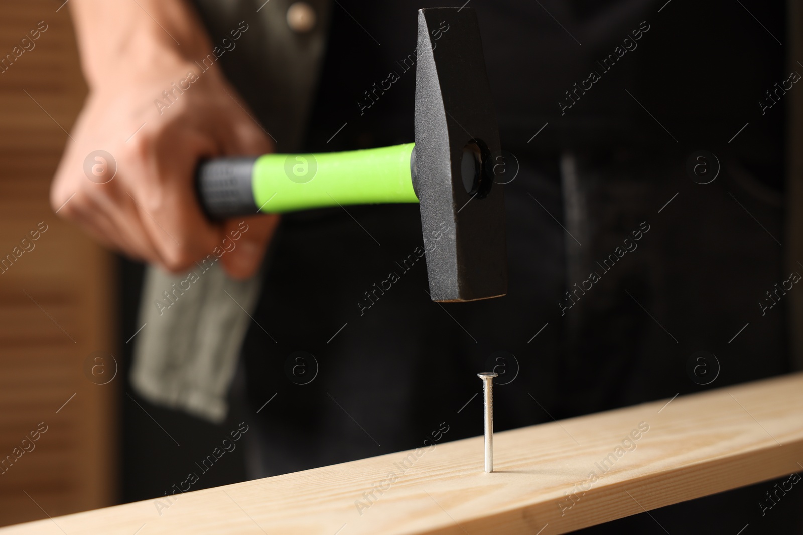 Photo of Man hammering nail into wooden plank indoors, closeup