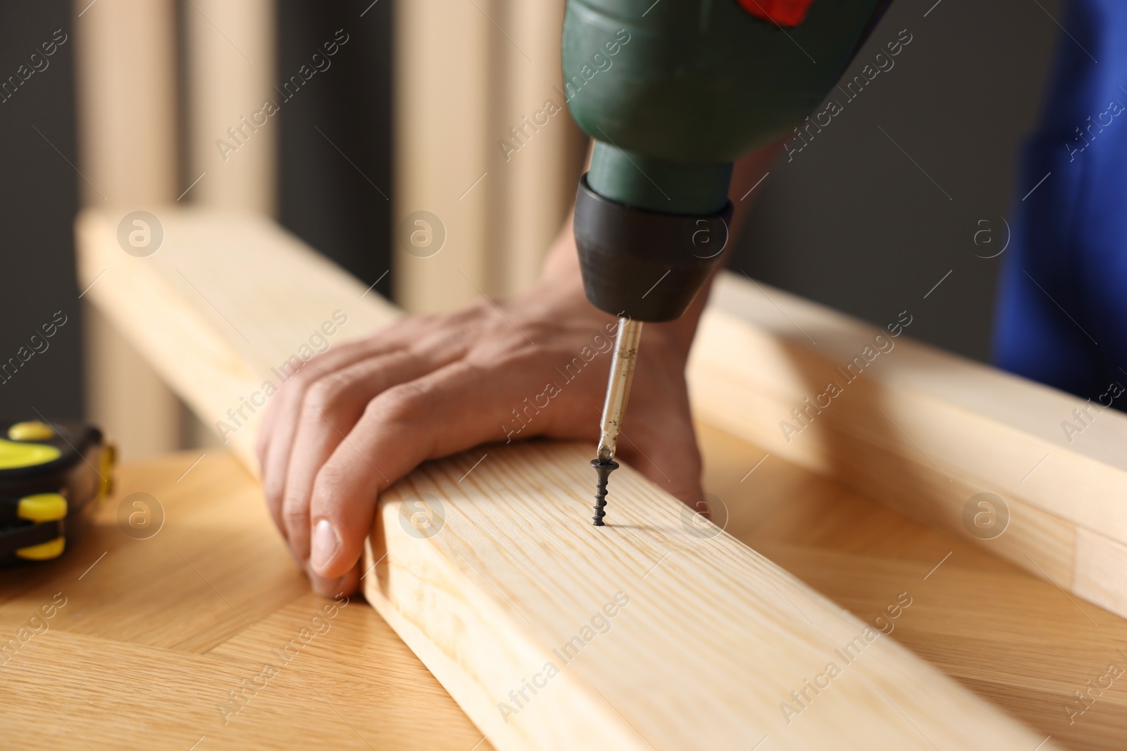 Professional repairman twisting screw into wooden plank with electric screwdriver indoors, closeup Photo of Professional repairman twisting screw into wooden plank with electric screwdriver indoors, closeup