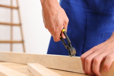 Photo of Professional repairman pulling nail out of wooden plank with pincers indoors, closeup