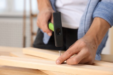 Photo of Man hammering nail into wooden plank indoors, closeup. Space for text